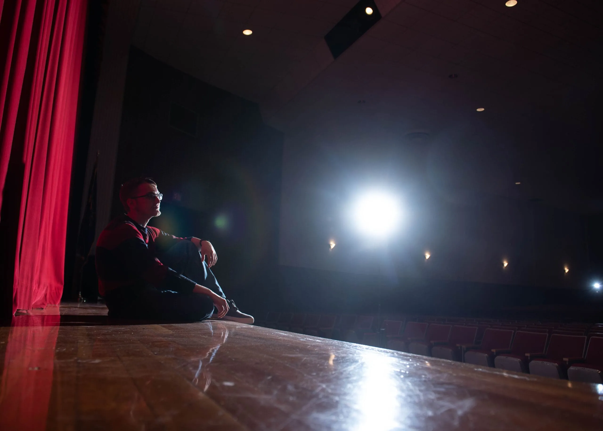 A performer seated on a theater stage under a spotlight